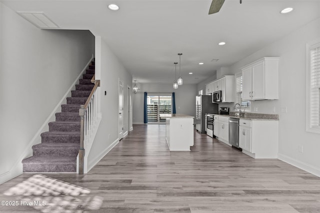 kitchen with a kitchen island, decorative light fixtures, white cabinets, light hardwood / wood-style floors, and stainless steel appliances