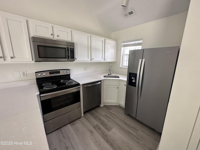 kitchen featuring appliances with stainless steel finishes, vaulted ceiling, sink, white cabinets, and light hardwood / wood-style floors