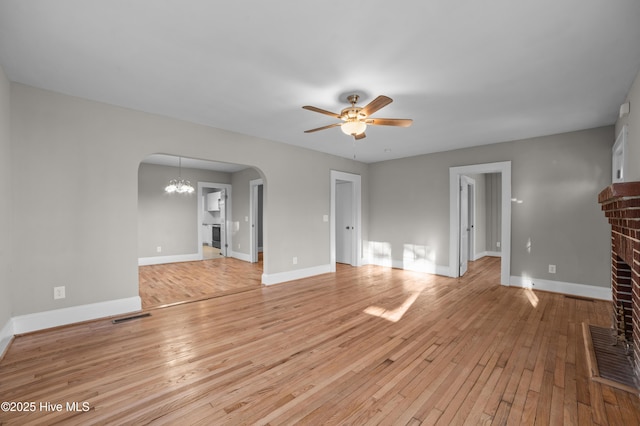 unfurnished living room with ceiling fan with notable chandelier, light hardwood / wood-style flooring, and a brick fireplace