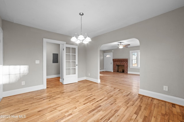 unfurnished dining area featuring ceiling fan with notable chandelier, light hardwood / wood-style floors, electric panel, and a brick fireplace