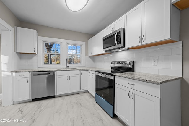 kitchen featuring white cabinetry, sink, light stone countertops, decorative backsplash, and appliances with stainless steel finishes