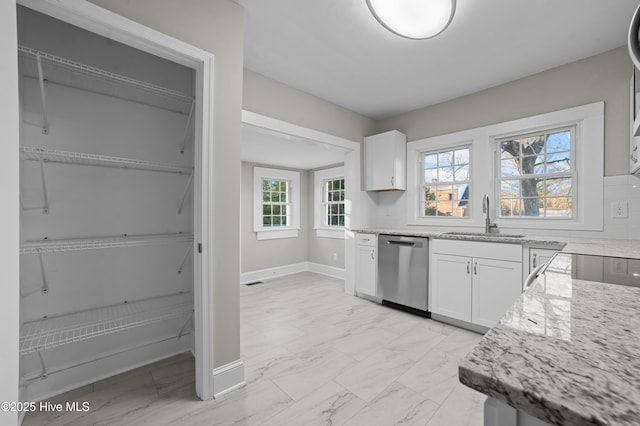 kitchen featuring stainless steel dishwasher, light stone counters, white cabinetry, and sink