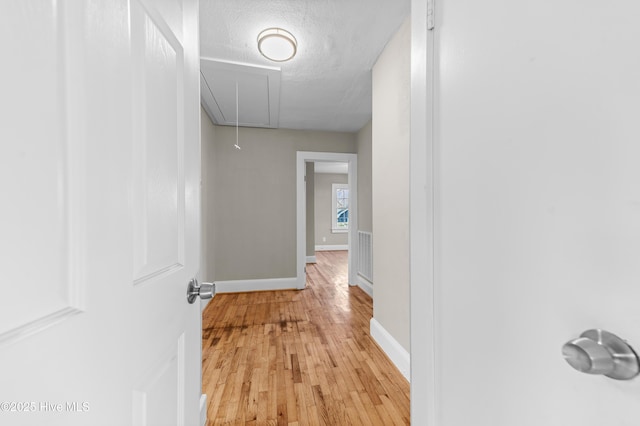 corridor with a textured ceiling and light hardwood / wood-style flooring