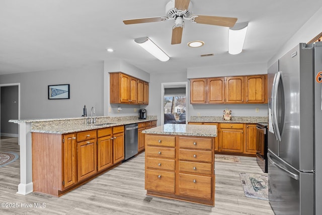 kitchen with sink, light stone counters, kitchen peninsula, a kitchen island, and stainless steel appliances