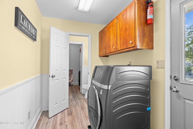 clothes washing area with washer / clothes dryer, cabinets, and light hardwood / wood-style floors