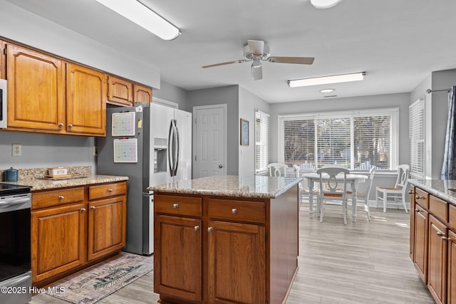 kitchen featuring ceiling fan, appliances with stainless steel finishes, a center island, light stone countertops, and light hardwood / wood-style floors