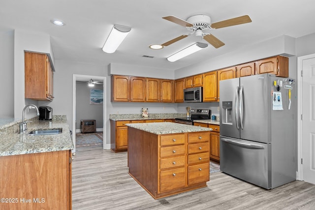 kitchen featuring sink, stainless steel appliances, a center island, light stone counters, and light wood-type flooring