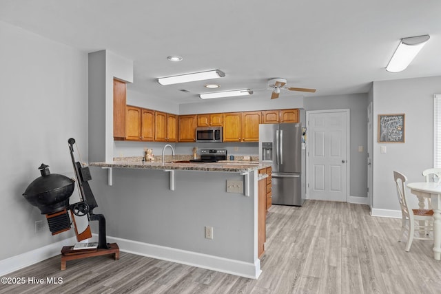 kitchen with light stone counters, a kitchen bar, light hardwood / wood-style floors, and appliances with stainless steel finishes