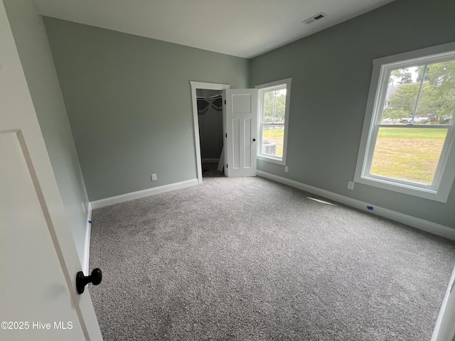 unfurnished bedroom featuring a closet, a walk in closet, carpet floors, and multiple windows