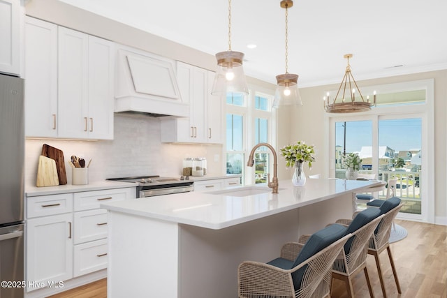 kitchen featuring sink, hanging light fixtures, custom range hood, and an island with sink