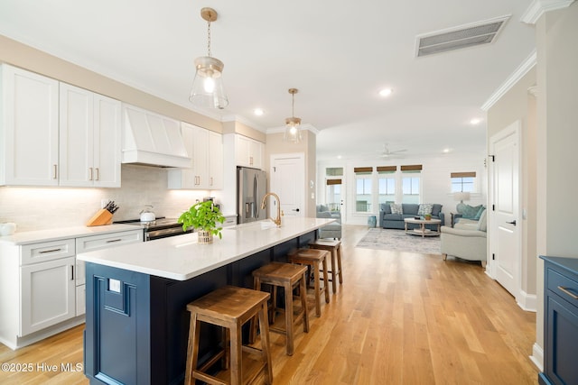 kitchen with a center island with sink, ceiling fan, white cabinetry, and premium range hood