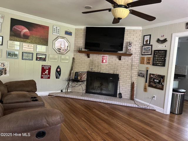 living room with hardwood / wood-style flooring, ceiling fan, ornamental molding, and a brick fireplace