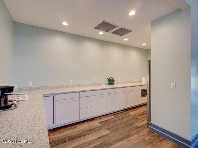 kitchen with white cabinets, stainless steel microwave, light stone countertops, and light hardwood / wood-style floors