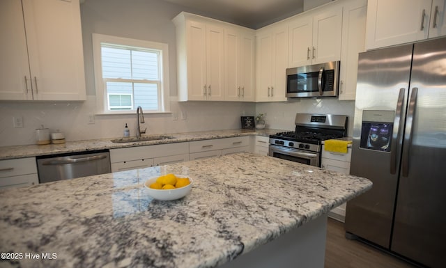 kitchen with appliances with stainless steel finishes, light stone counters, white cabinetry, and sink