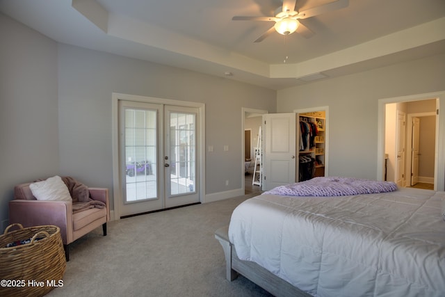 bedroom with french doors, a walk in closet, a tray ceiling, and ceiling fan