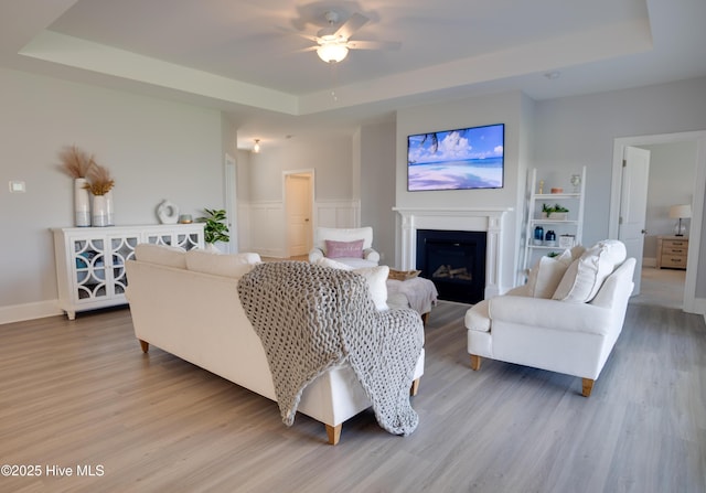 living room featuring a tray ceiling, built in shelves, ceiling fan, and wood-type flooring