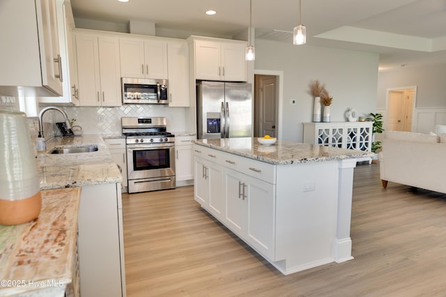 kitchen with a center island, white cabinets, sink, hanging light fixtures, and appliances with stainless steel finishes