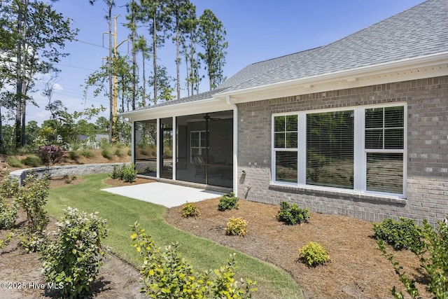 exterior space featuring roof with shingles, brick siding, a sunroom, a patio, and a yard