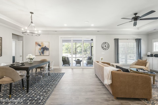 living room featuring ceiling fan with notable chandelier, a tray ceiling, crown molding, and wood finished floors