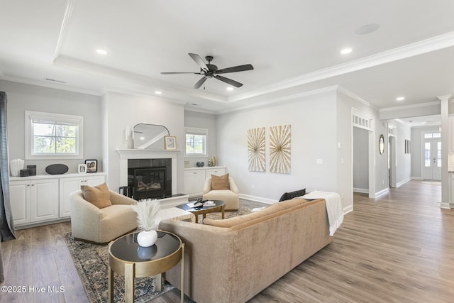 living area with a fireplace, light wood-style floors, ceiling fan, and a raised ceiling
