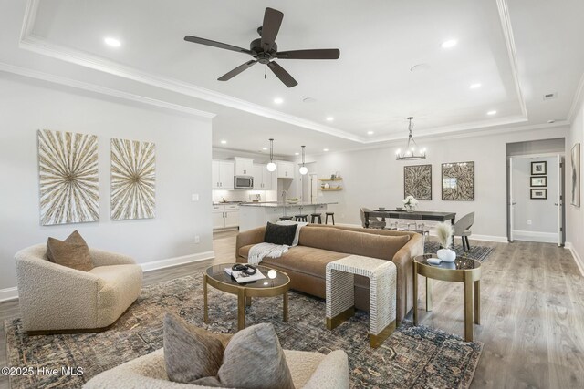 carpeted bedroom with a tray ceiling, ceiling fan, ensuite bathroom, and ornamental molding