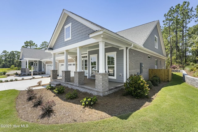 view of side of property with driveway, covered porch, roof with shingles, brick siding, and a lawn