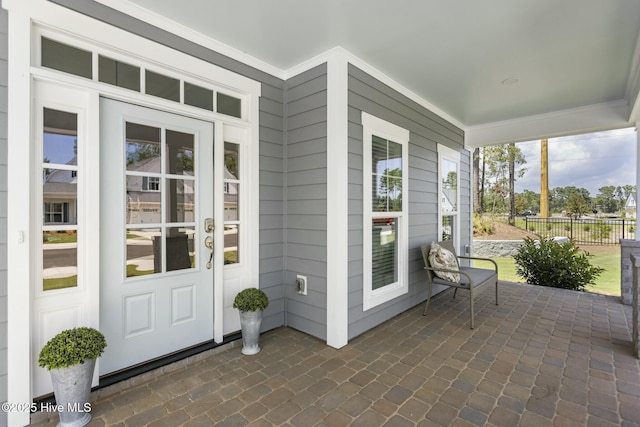 view of exterior entry with covered porch and fence