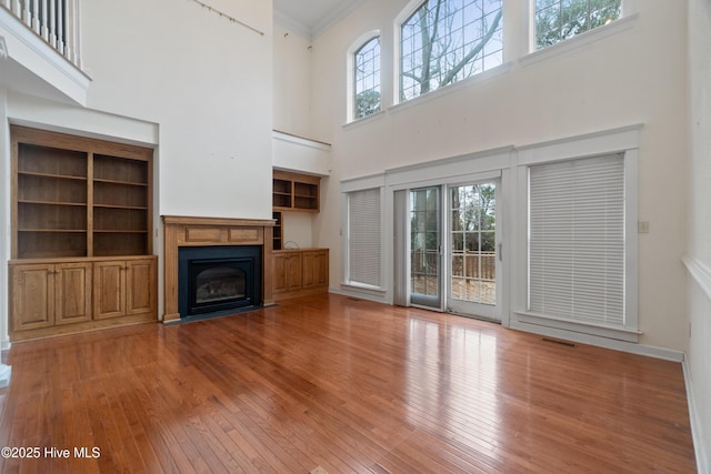 unfurnished living room featuring built in shelves, a towering ceiling, and wood-type flooring