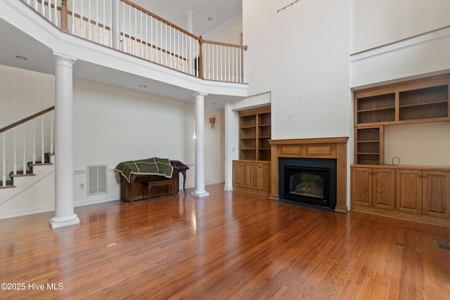 unfurnished living room with hardwood / wood-style floors, built in shelves, and a towering ceiling