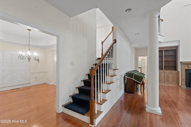 stairs featuring hardwood / wood-style flooring, ornate columns, and an inviting chandelier