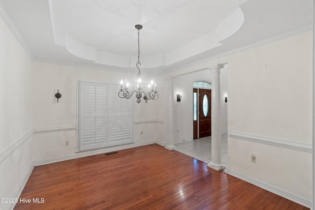 unfurnished dining area featuring hardwood / wood-style floors, a tray ceiling, decorative columns, and a notable chandelier