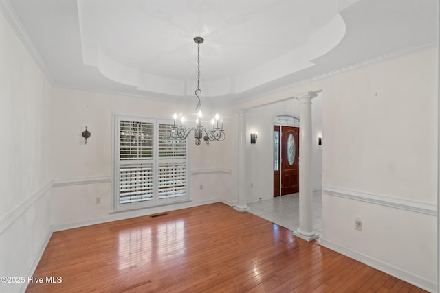 unfurnished dining area with hardwood / wood-style floors, decorative columns, a raised ceiling, and a notable chandelier