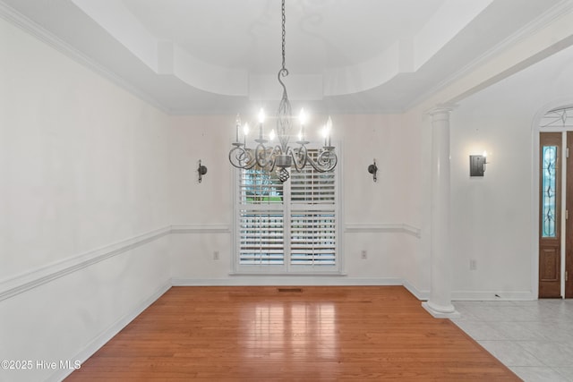 unfurnished dining area with a raised ceiling, decorative columns, a notable chandelier, and tile patterned flooring