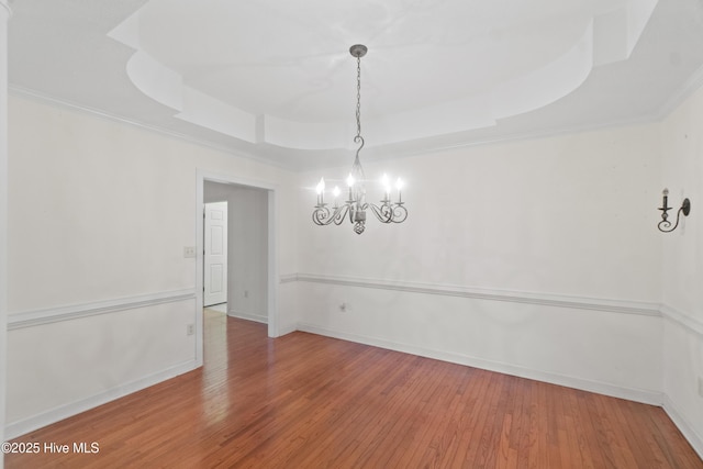 empty room featuring a notable chandelier, wood-type flooring, and a tray ceiling