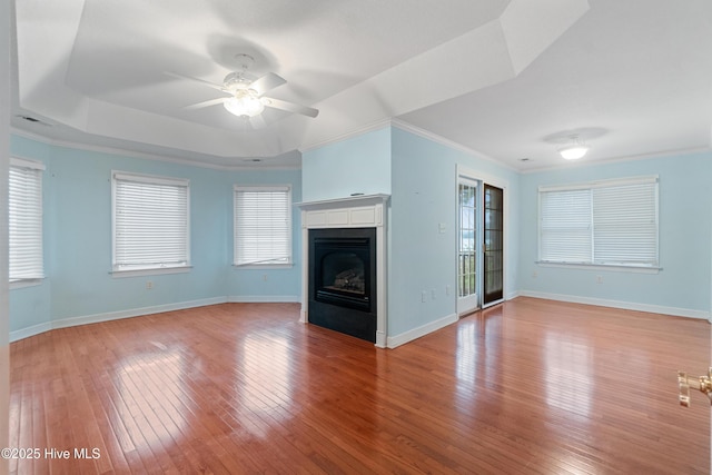 unfurnished living room featuring hardwood / wood-style floors, ceiling fan, a raised ceiling, and crown molding