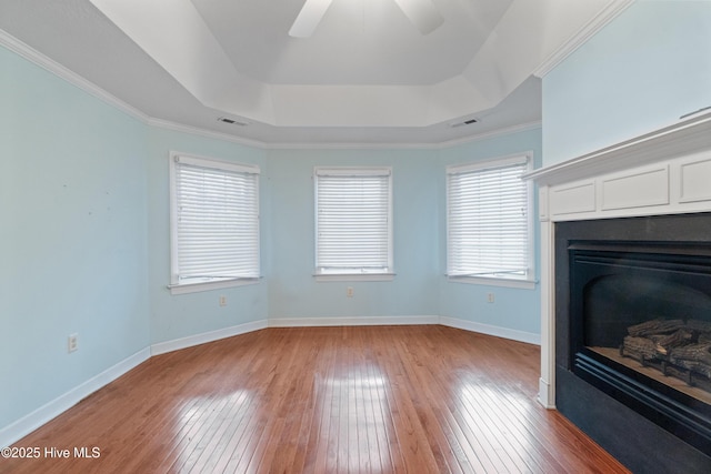 unfurnished living room featuring ceiling fan, ornamental molding, light hardwood / wood-style flooring, and a tray ceiling