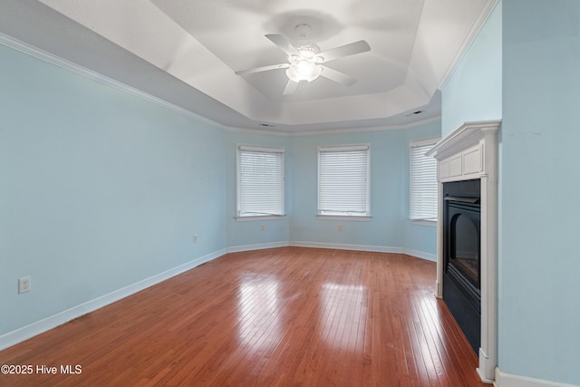 unfurnished living room featuring a tray ceiling, ceiling fan, crown molding, and hardwood / wood-style flooring