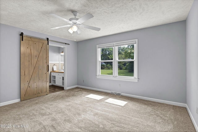 unfurnished bedroom with carpet flooring, ensuite bath, a textured ceiling, ceiling fan, and a barn door