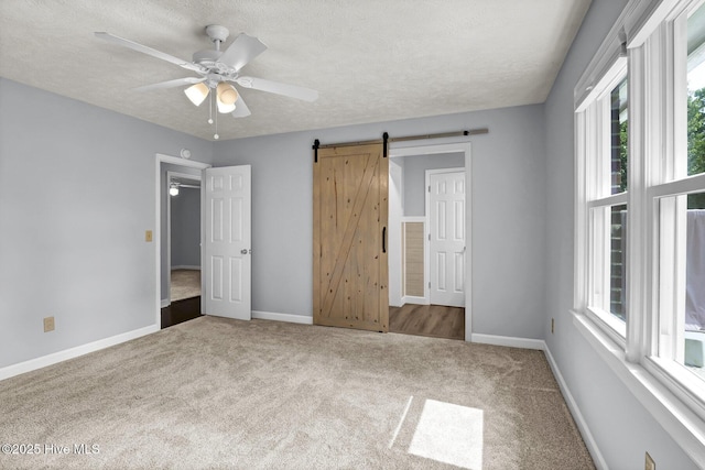 unfurnished bedroom with carpet flooring, ceiling fan, a barn door, and a textured ceiling