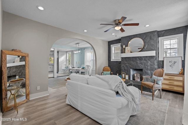 living room featuring a wealth of natural light, a fireplace, ceiling fan, and light wood-type flooring