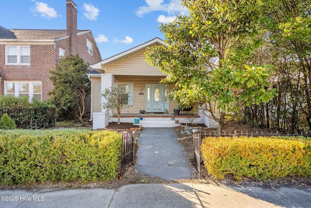 view of front of home with covered porch, a fenced front yard, and a chimney