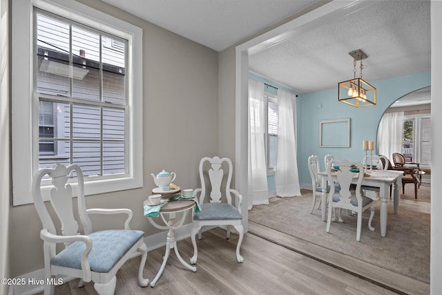 dining space with hardwood / wood-style flooring, a wealth of natural light, a notable chandelier, and a textured ceiling