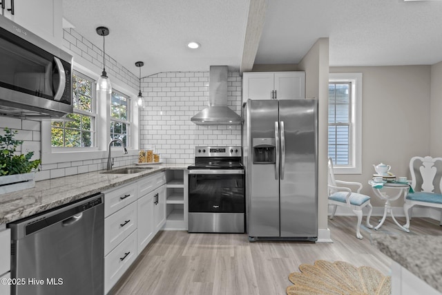 kitchen featuring wall chimney range hood, sink, appliances with stainless steel finishes, white cabinetry, and a textured ceiling