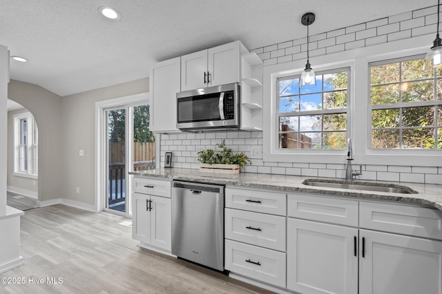 kitchen with sink, white cabinets, pendant lighting, stainless steel appliances, and backsplash