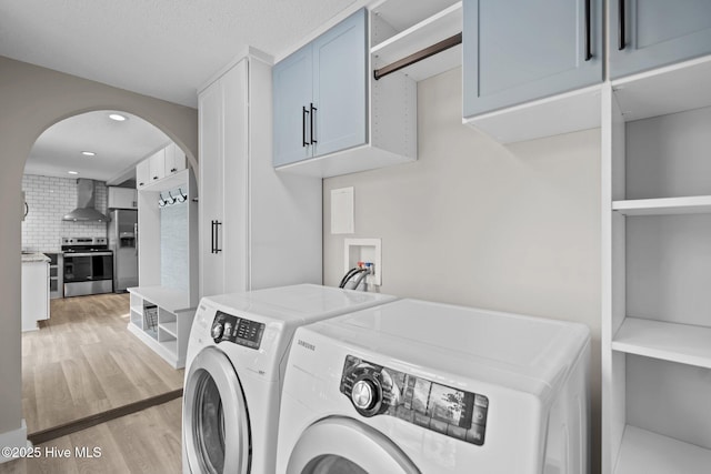 clothes washing area with cabinets, washing machine and clothes dryer, light hardwood / wood-style floors, and a textured ceiling