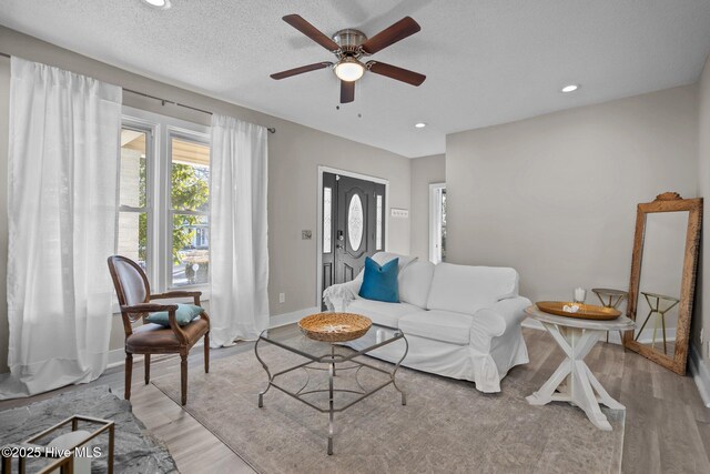 living room with ceiling fan, light hardwood / wood-style flooring, and a textured ceiling