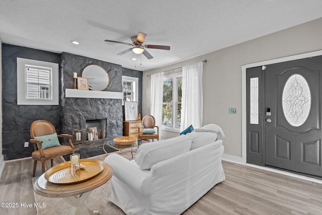 living room featuring ceiling fan, a stone fireplace, wood-type flooring, and a textured ceiling