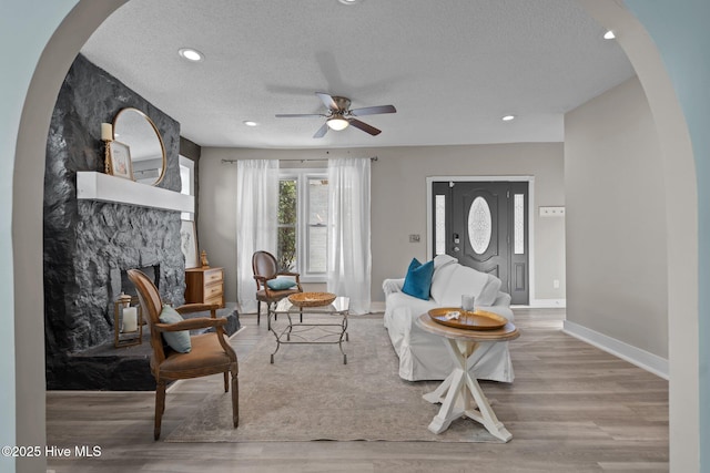 living area featuring ceiling fan, a textured ceiling, a fireplace, and light hardwood / wood-style flooring