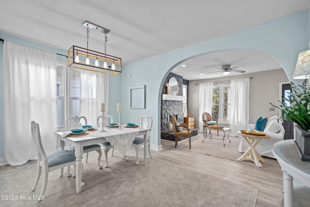 dining area with ceiling fan, a fireplace, light hardwood / wood-style floors, and a textured ceiling