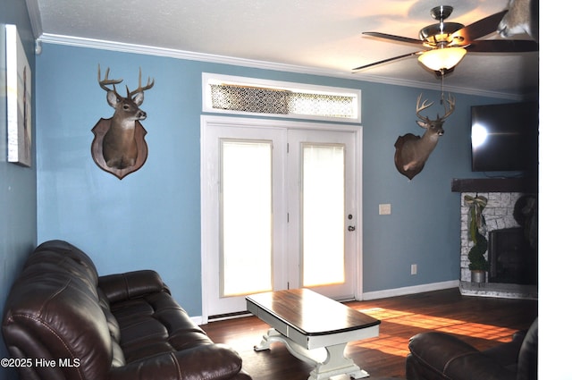 living room featuring dark wood-type flooring, a stone fireplace, ceiling fan, and ornamental molding